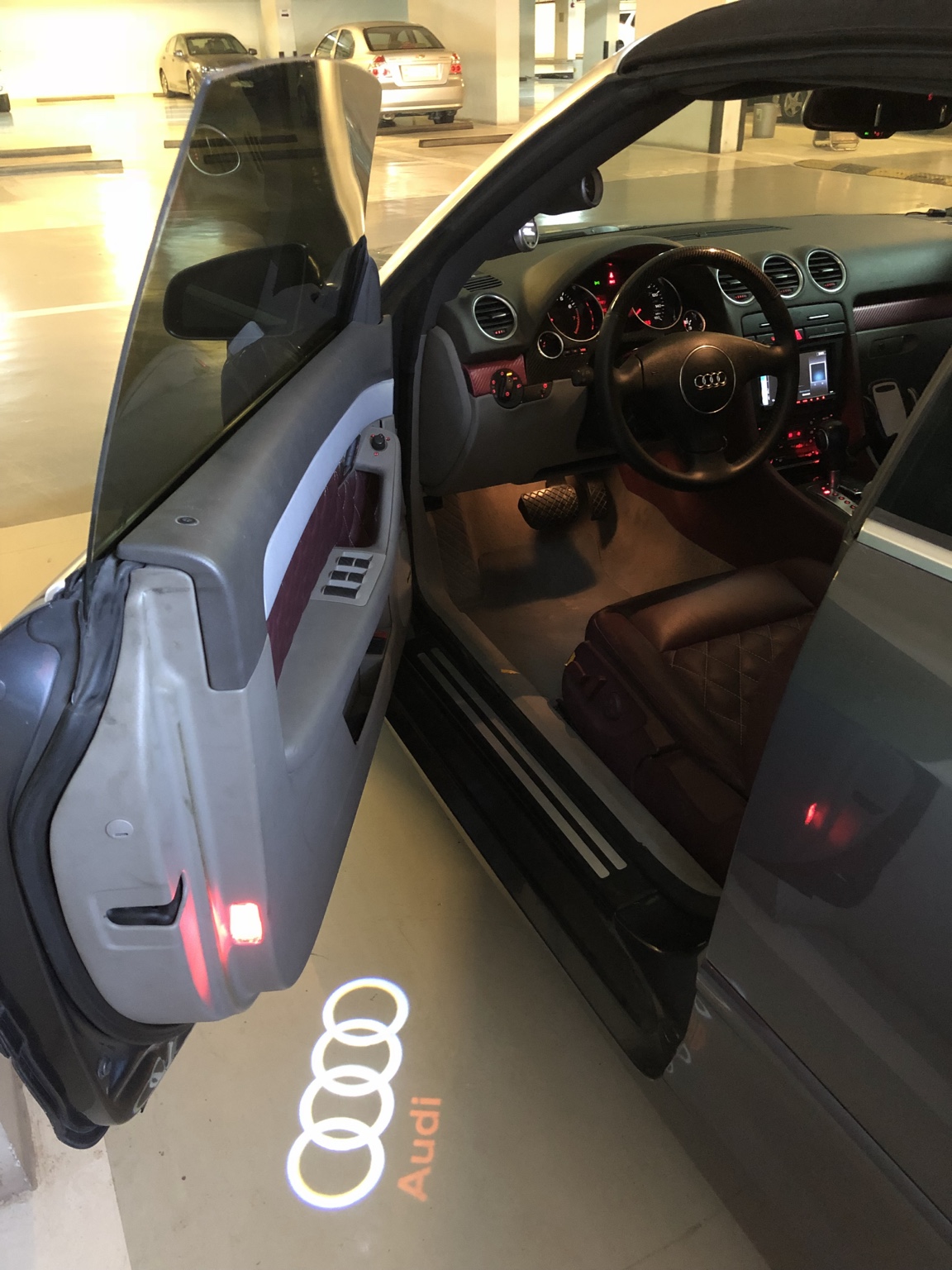 Personalized Audi Cabriolet interior with the driver's door open and puddle light illuminated